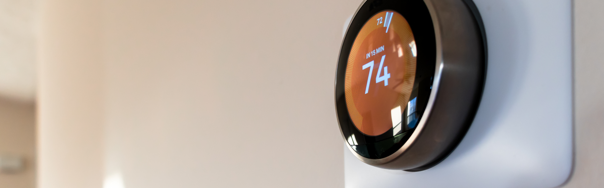 A round smart thermostat mounted on a wall displays a temperature setting of 74 degrees.