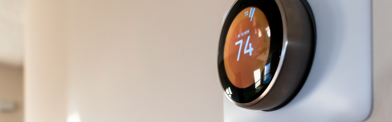 A round smart thermostat mounted on a wall displays a temperature setting of 74 degrees.
