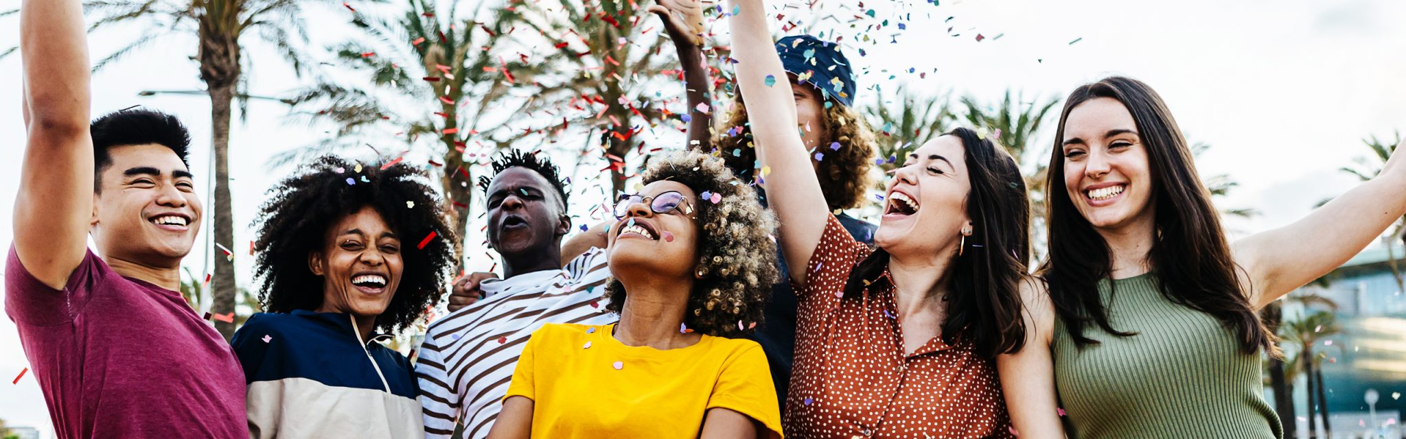 A group of six people smile and celebrate outdoors with confetti at a Valley Clean Energy Events gathering under sunny palm trees.