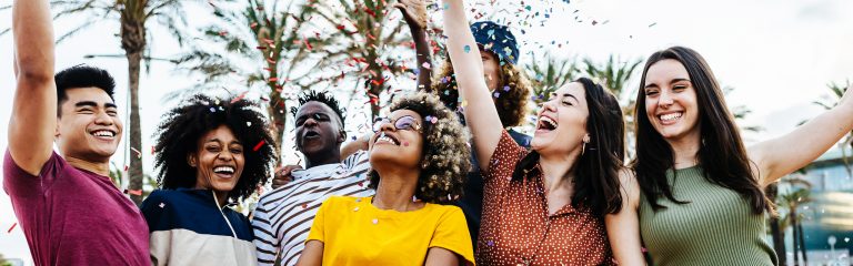 A group of six people smile and celebrate outdoors with confetti at a Valley Clean Energy Events gathering under sunny palm trees.