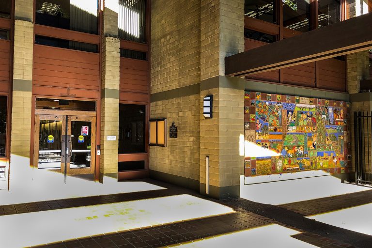 Entrance to a brick building with glass doors and a colorful mural displayed on the wall to the right of the entrance.