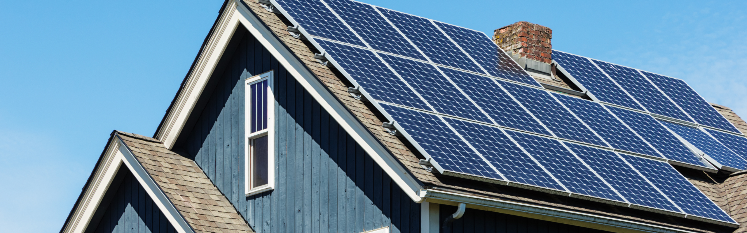 Blue house roof with multiple solar panels installed, chimney visible, set against a clear blue sky.